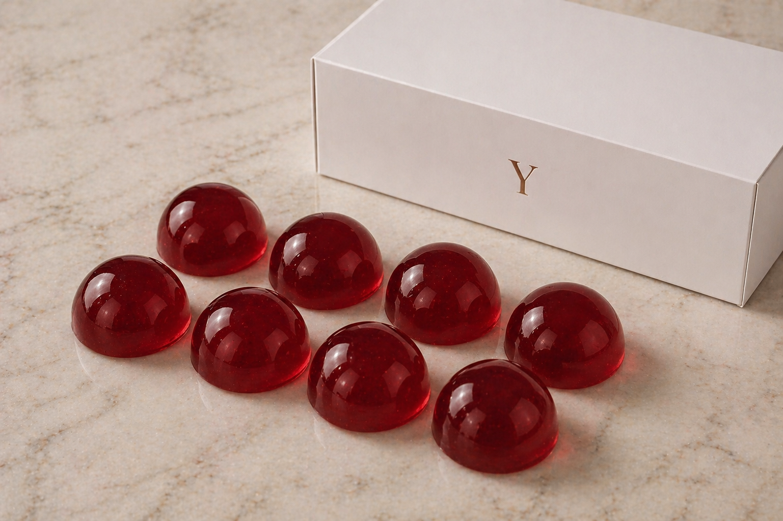 Eight smooth deep red jelly shot domes displayed on a marble surface beside a luxury white YIXO gift box with gold Y detail.